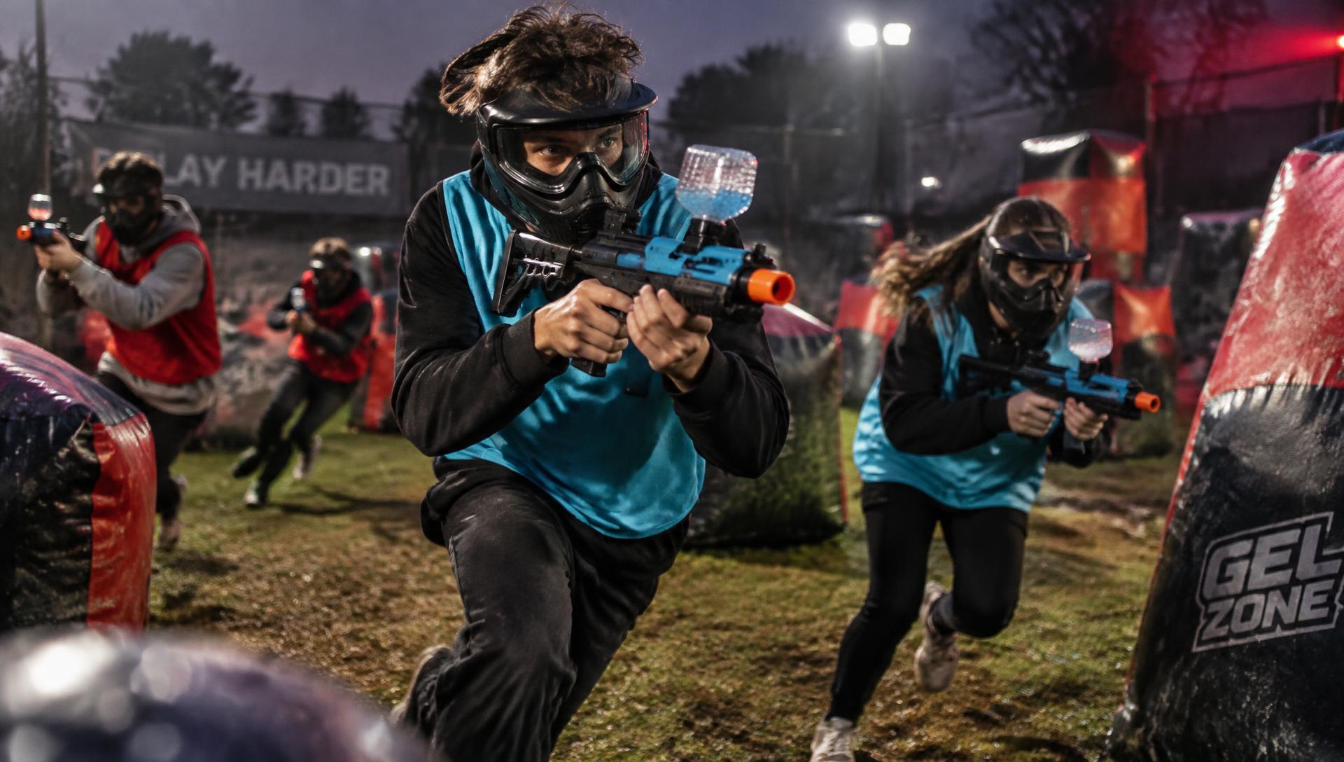 Children in protective face masks playing an organised Gel Blaster team game outdoors